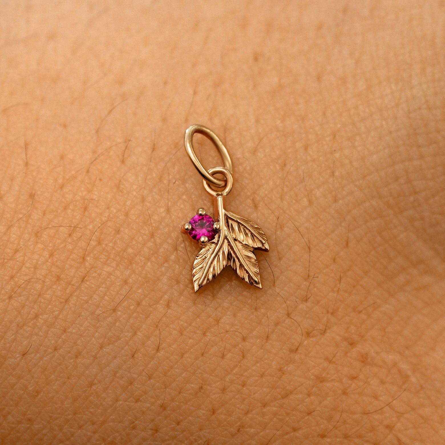 A solid 14k rose gold ruby Gemstone 3 Leaves Charm resting on the back of a model's hand
