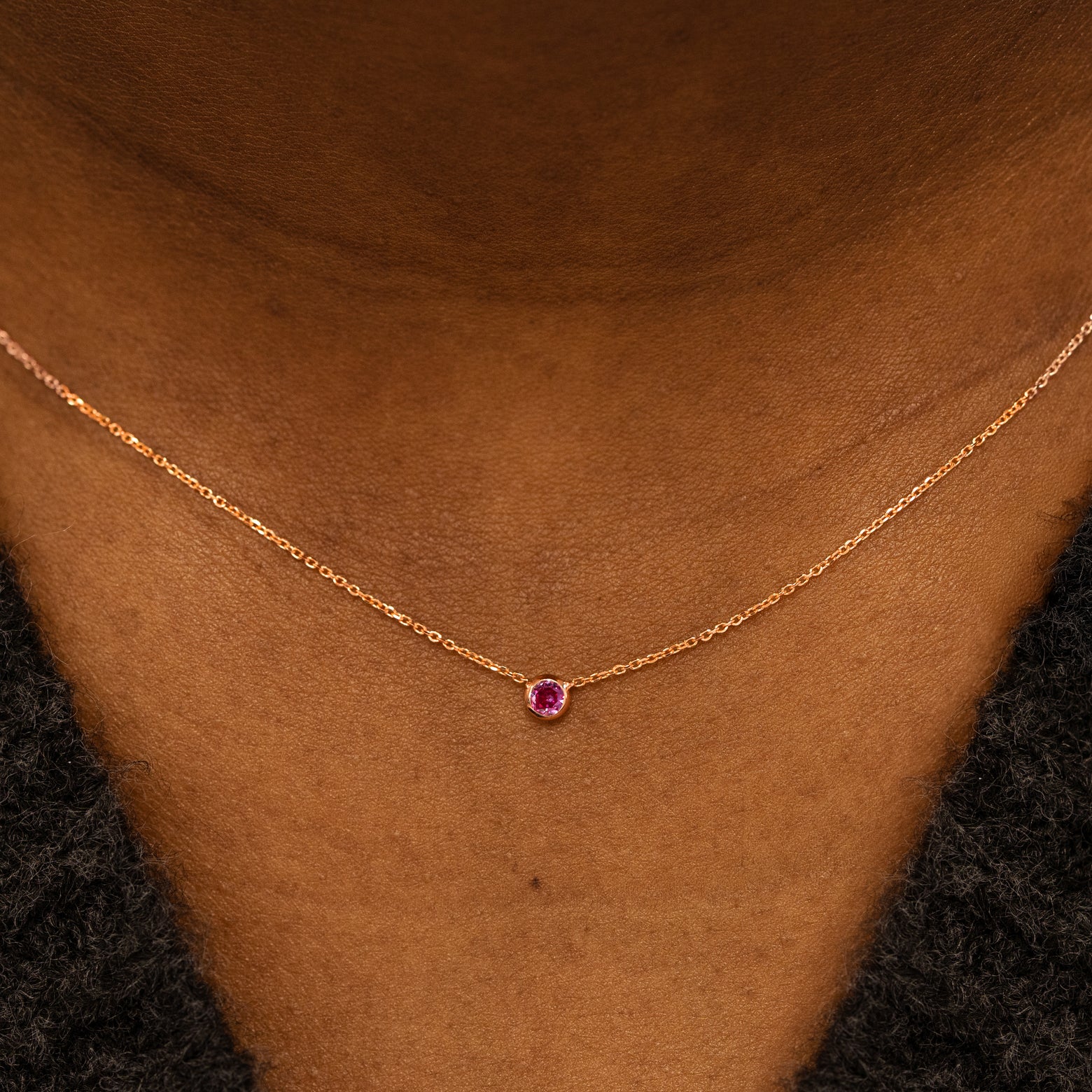 Close up view of a model neck wearing a 14k rose gold Bezel set gemstone necklace in pink sapphire