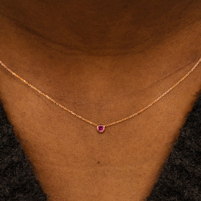 Close up view of a model neck wearing a 14k rose gold Bezel set gemstone necklace in pink sapphire