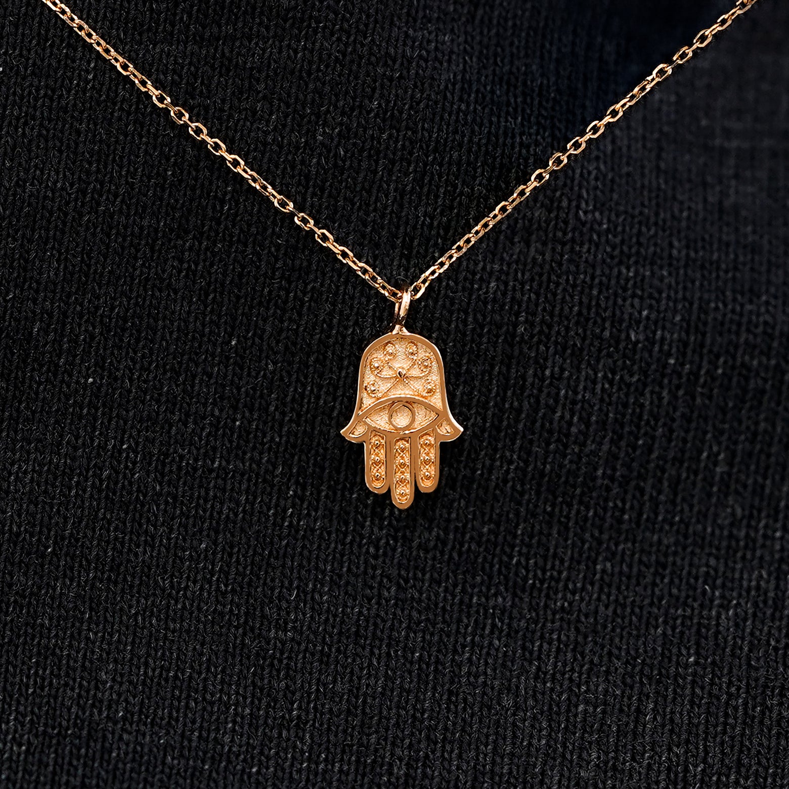 Close up view of a solid 14k rose gold hamsa necklace against a model's black shirt