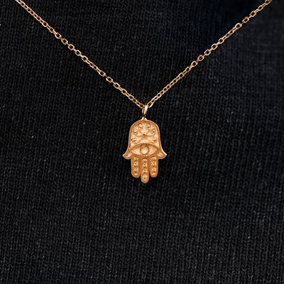 Close up view of a solid 14k rose gold hamsa necklace against a model's black shirt