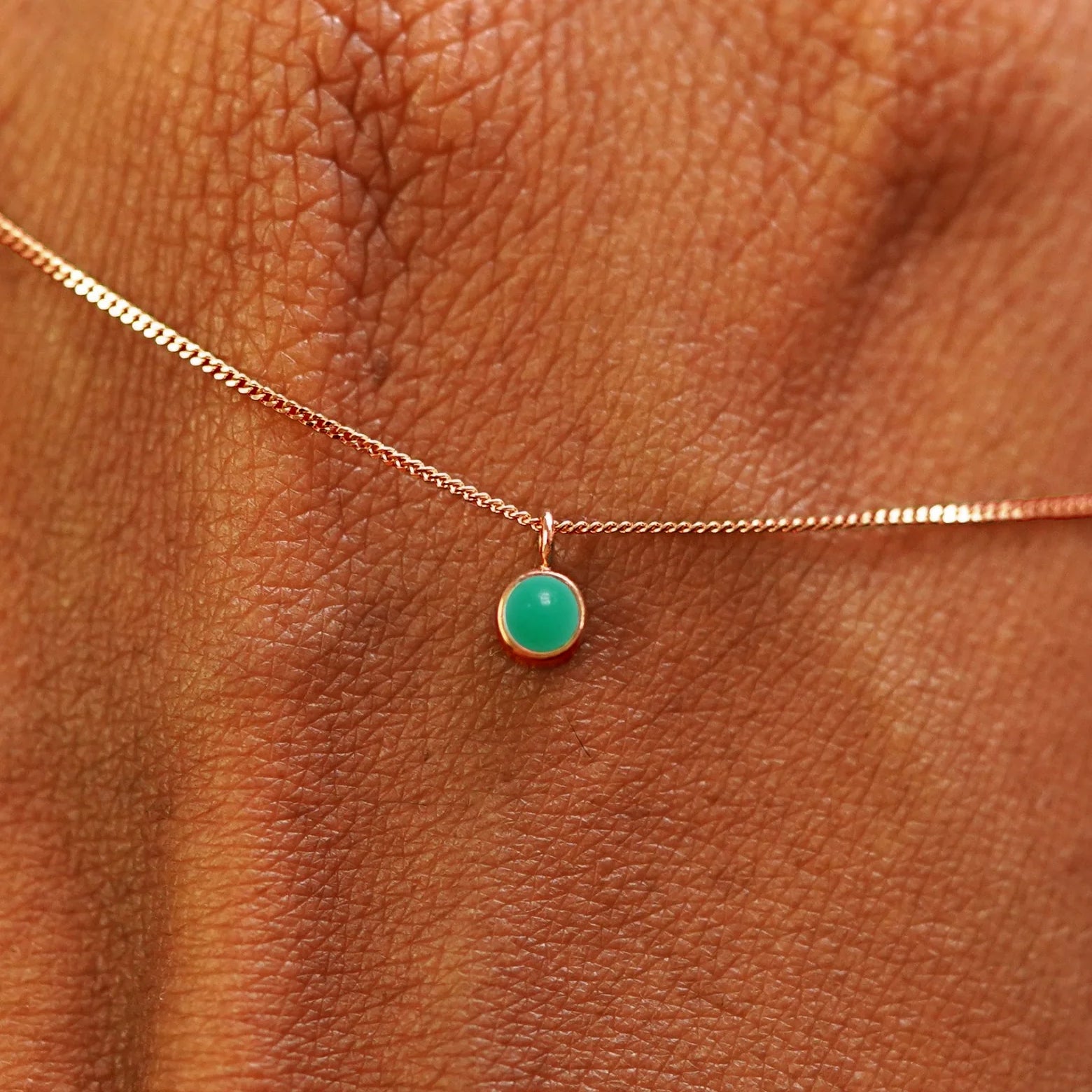 Close up view of a 14k rose gold Jade Necklace draped across the back of a model's hand