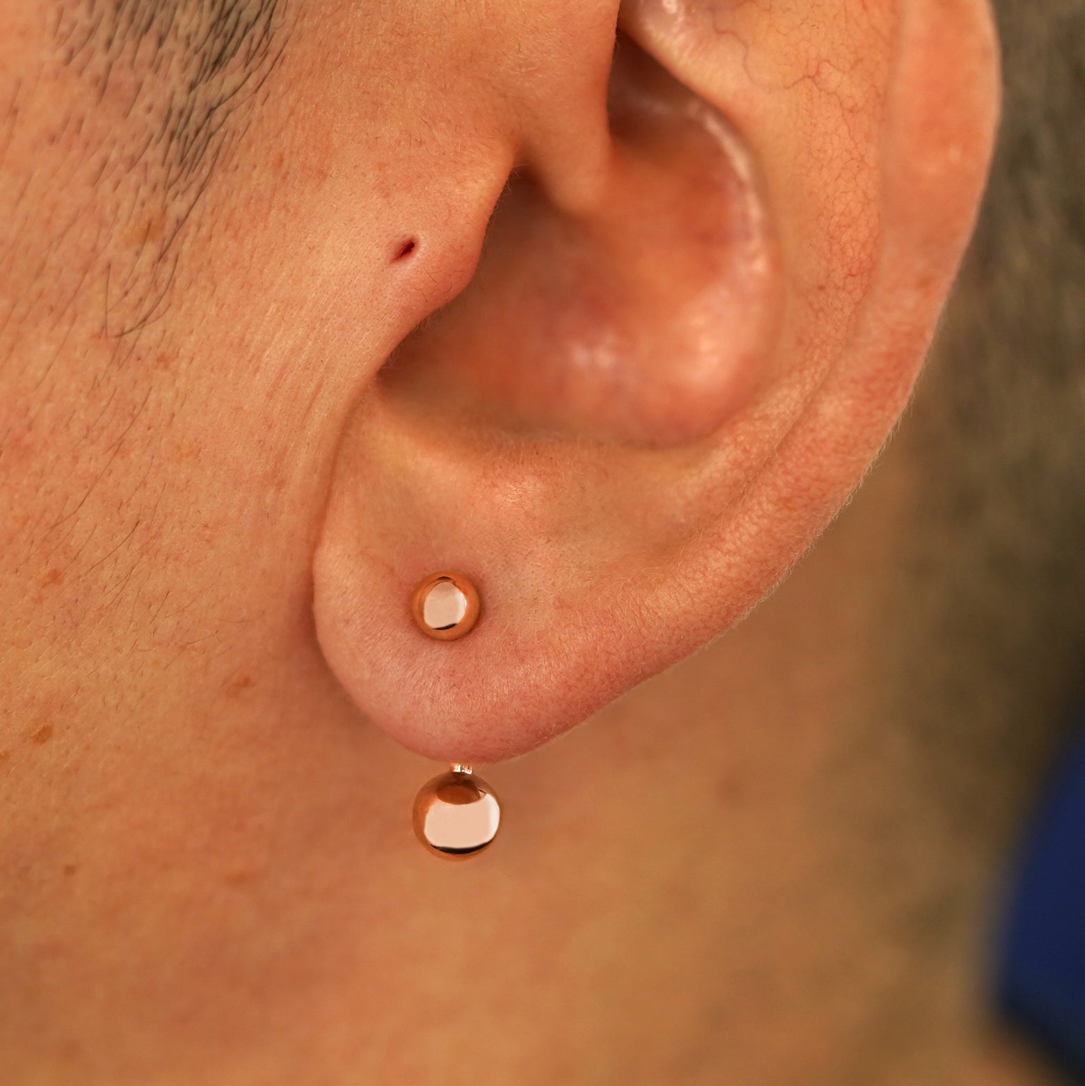 Close up view of a model's ear wearing a 14k rose gold Large Curved Barbell through a lobe piercing