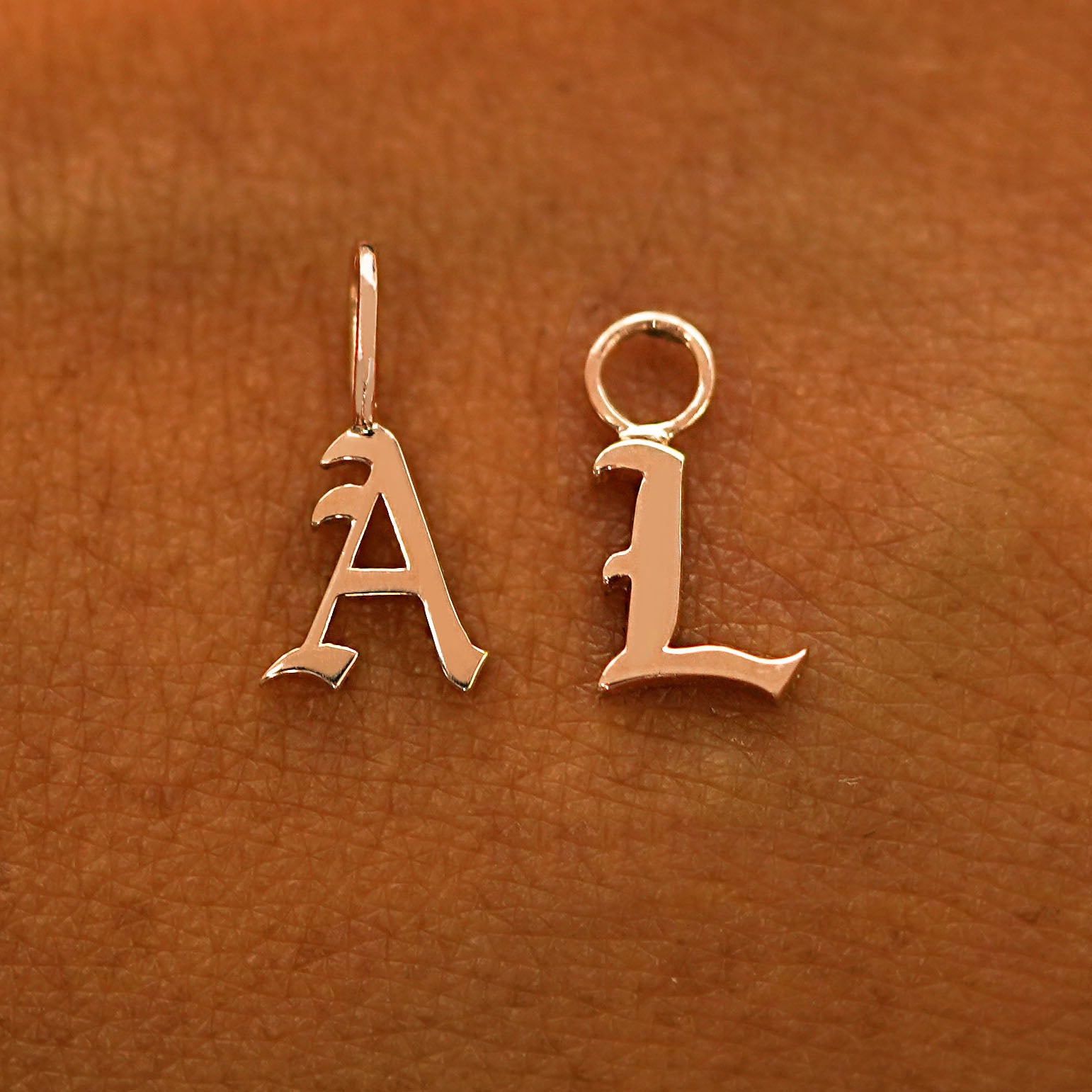 A solid 14k rose gold Initial Charm for earring in the letter A and L laying on the back of a model's hand