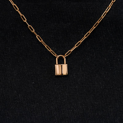 Close up view of a solid 14k rose gold lock necklace against a model's black shirt