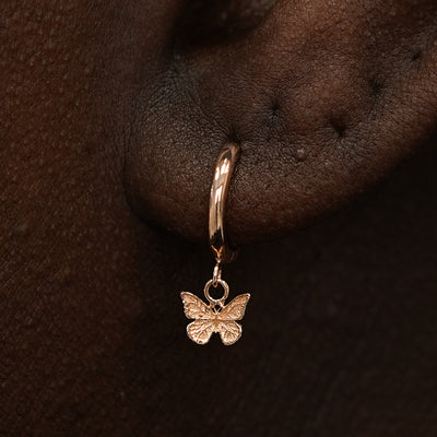 Close up view of a model's ear wearing a rose gold Mini Butterfly Dangle Huggie Hoop