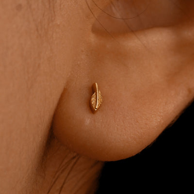 Close up view of a model's ear wearing a 14k rose gold Mini Leaf Flatback Piercing 