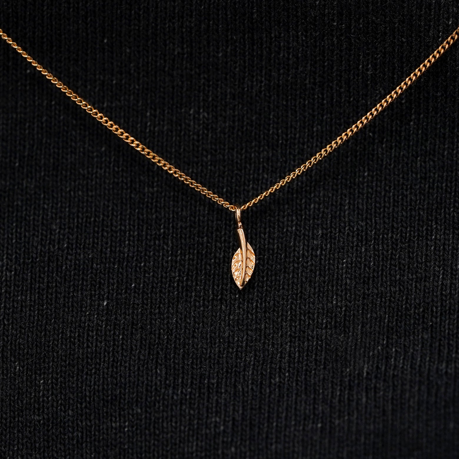 Close up view of a solid 14k rose gold mini leaf necklace against a model's black shirt