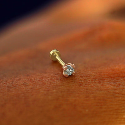 A solid 14k rose gold Moissanite Flatback Piercing resting on the back of a model's hand