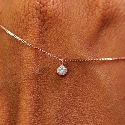 Close up view of a 14k rose gold Moissanite Necklace draped across the back of a model's hand