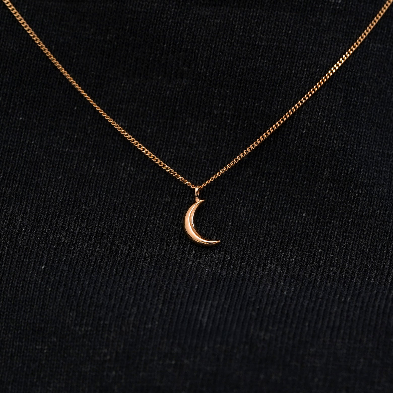 Close up view of a solid 14k rose gold moon necklace against a model's black shirt
