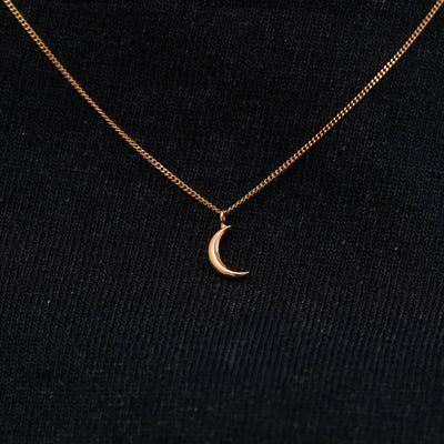 Close up view of a solid 14k rose gold moon necklace against a model's black shirt