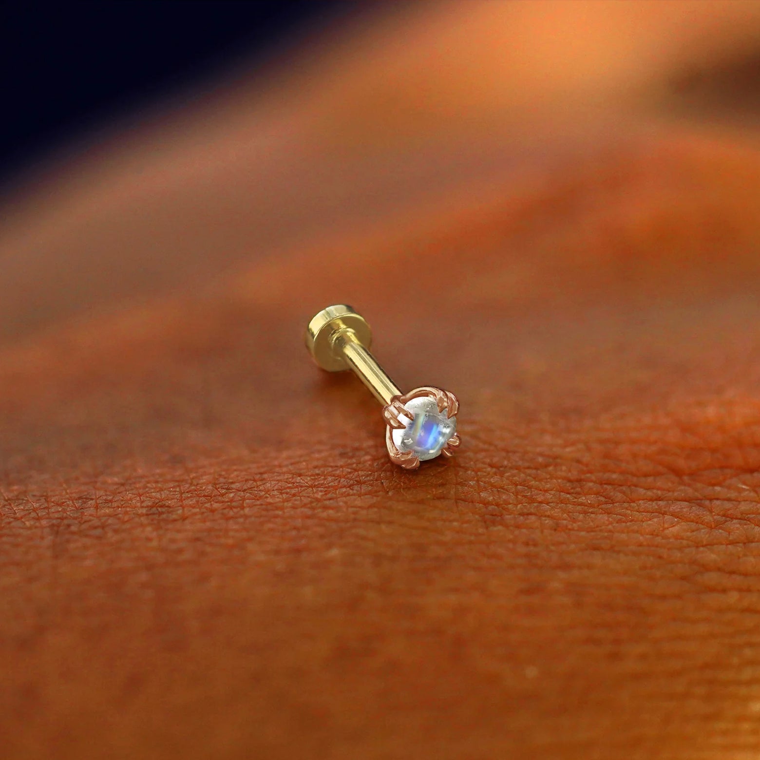 A solid 14k rose gold Moonstone Flatback Piercing resting on the back of a model's hand