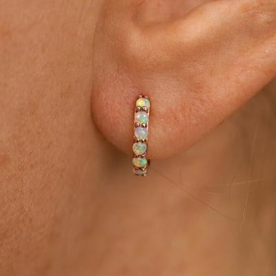 Close up view of a model's ear wearing a rose gold Small Opal Huggie Hoop