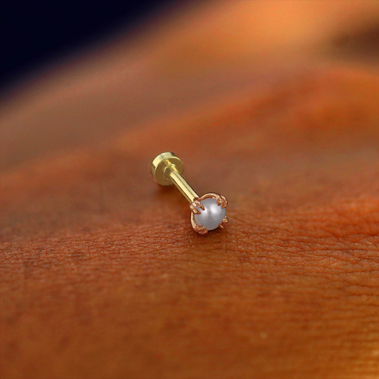 A solid 14k rose gold Pearl Flatback Piercing resting on the back of a model's hand