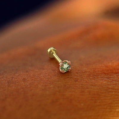 A solid 14k rose gold Peridot Flatback Piercing resting on the back of a model's hand