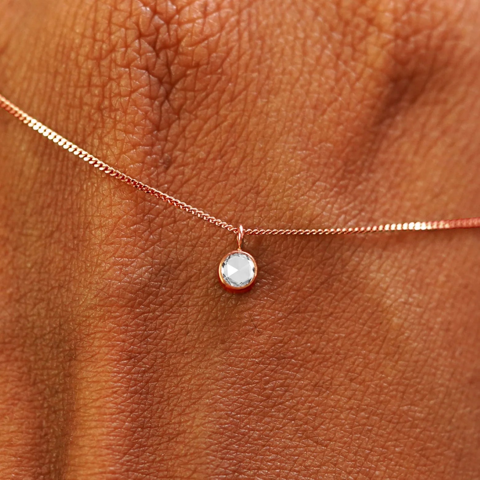 Close up view of a 14k rose gold Rose Cut Diamond Necklace draped across the back of a model's hand