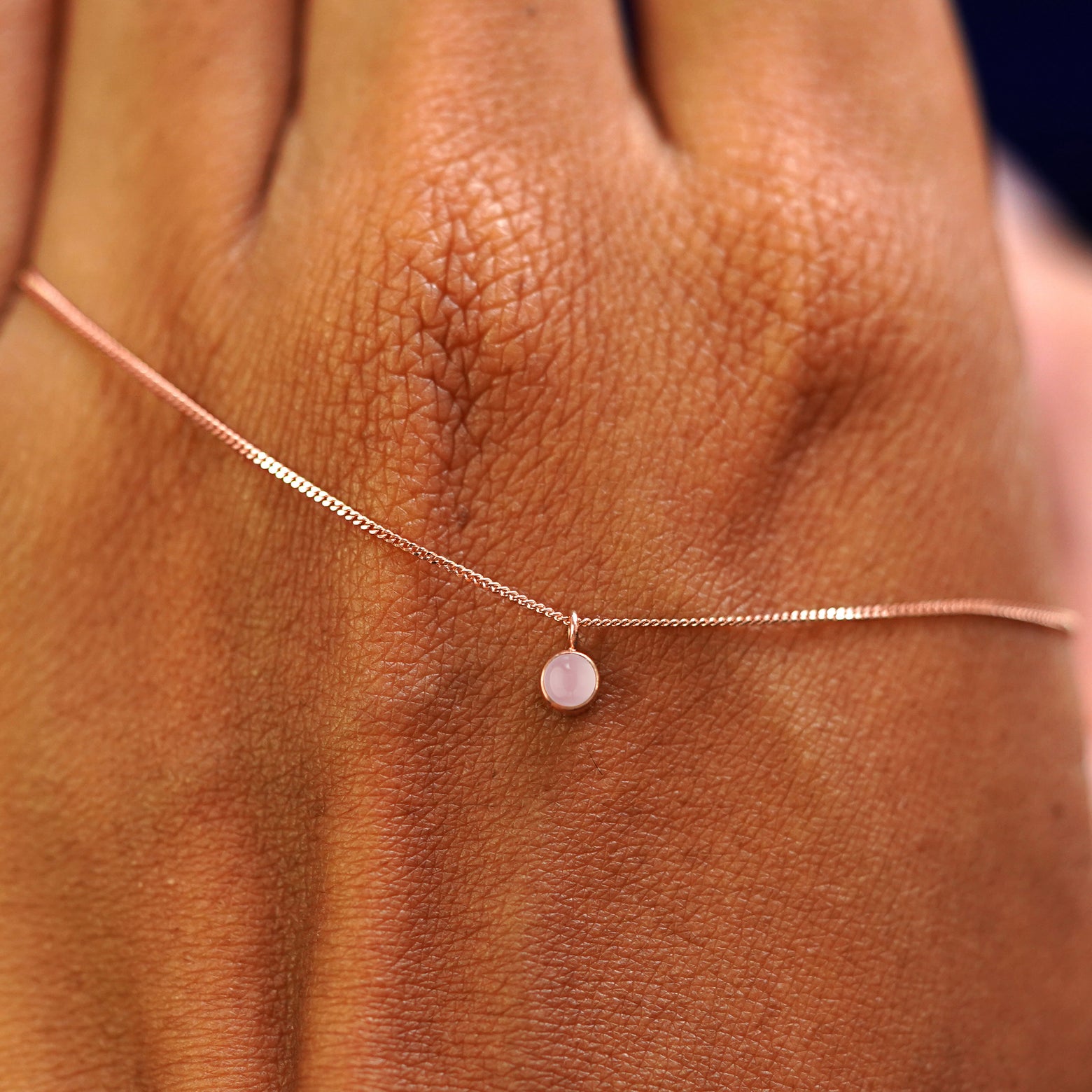 A solid rose gold Rose Quartz Necklace draped across the back of a model's hand