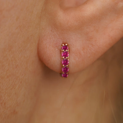 Close up view of a model's ear wearing a rose gold Mini Ruby Huggie Hoop