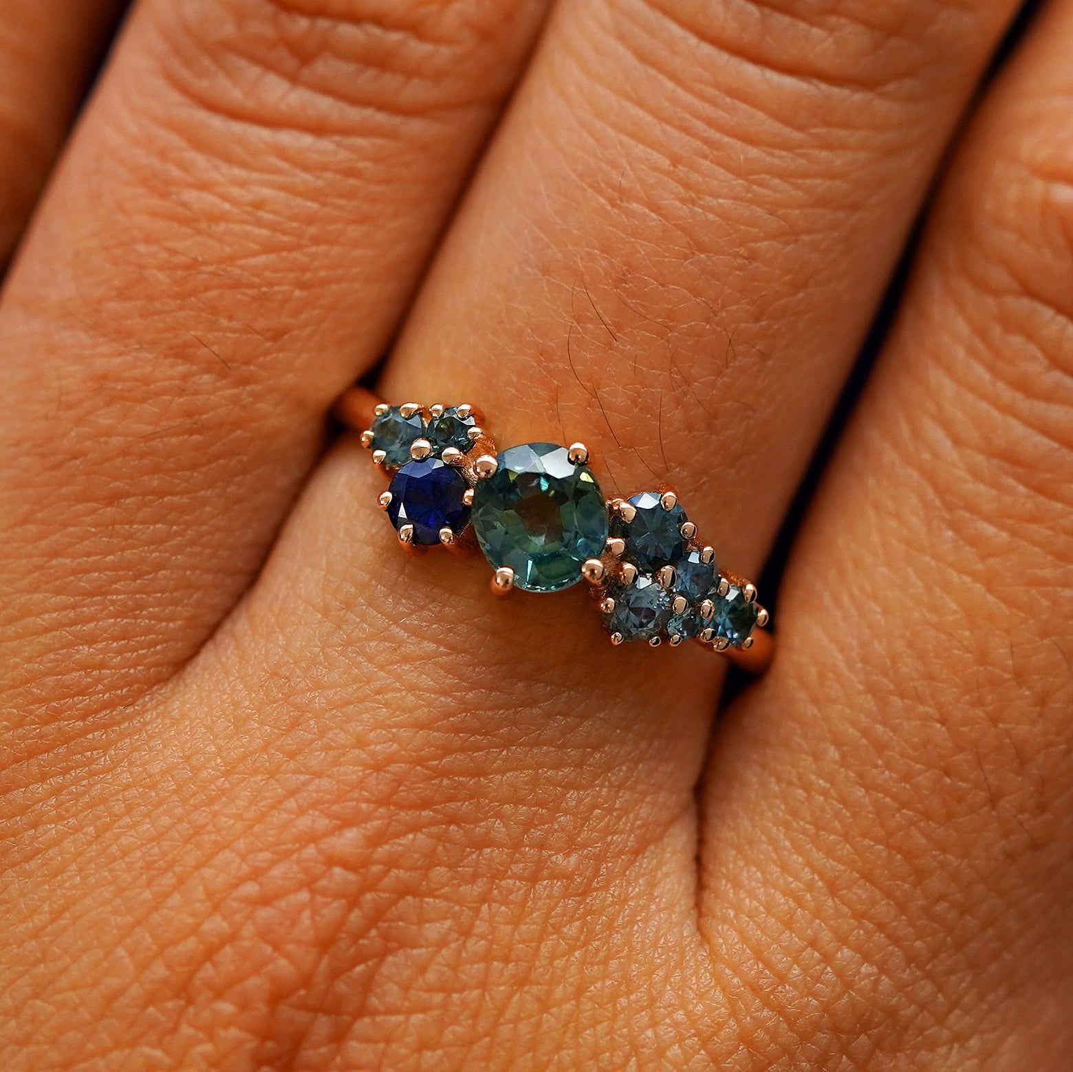 Close up view of a model's hand wearing a 14k rose gold sapphire cluster ring
