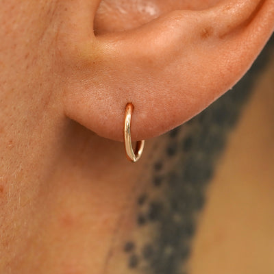 A model's ear wearing a 14k rose gold Small Seamless Huggie Hoop / Piercing