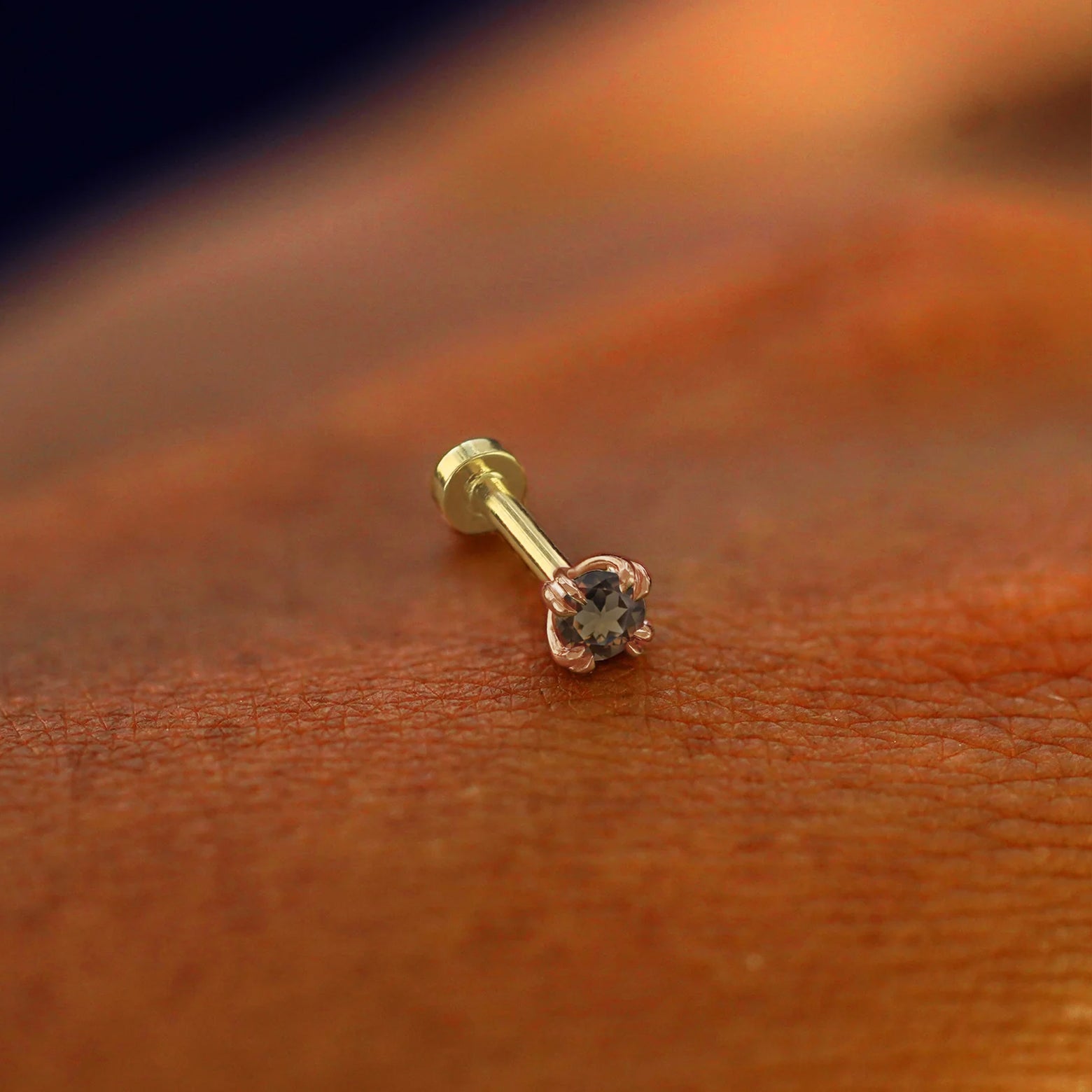 A solid 14k rose gold Smoky Quartz Flatback Piercing resting on the back of a model's hand