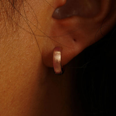 Close up view of a model's ear wearing a 14k rose gold Stardust Small Wide Huggie Hoops
