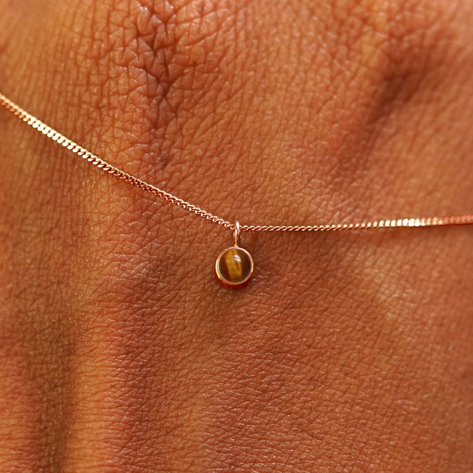Close up view of a 14k rose gold Tiger Eye Necklace draped across the back of a model's hand