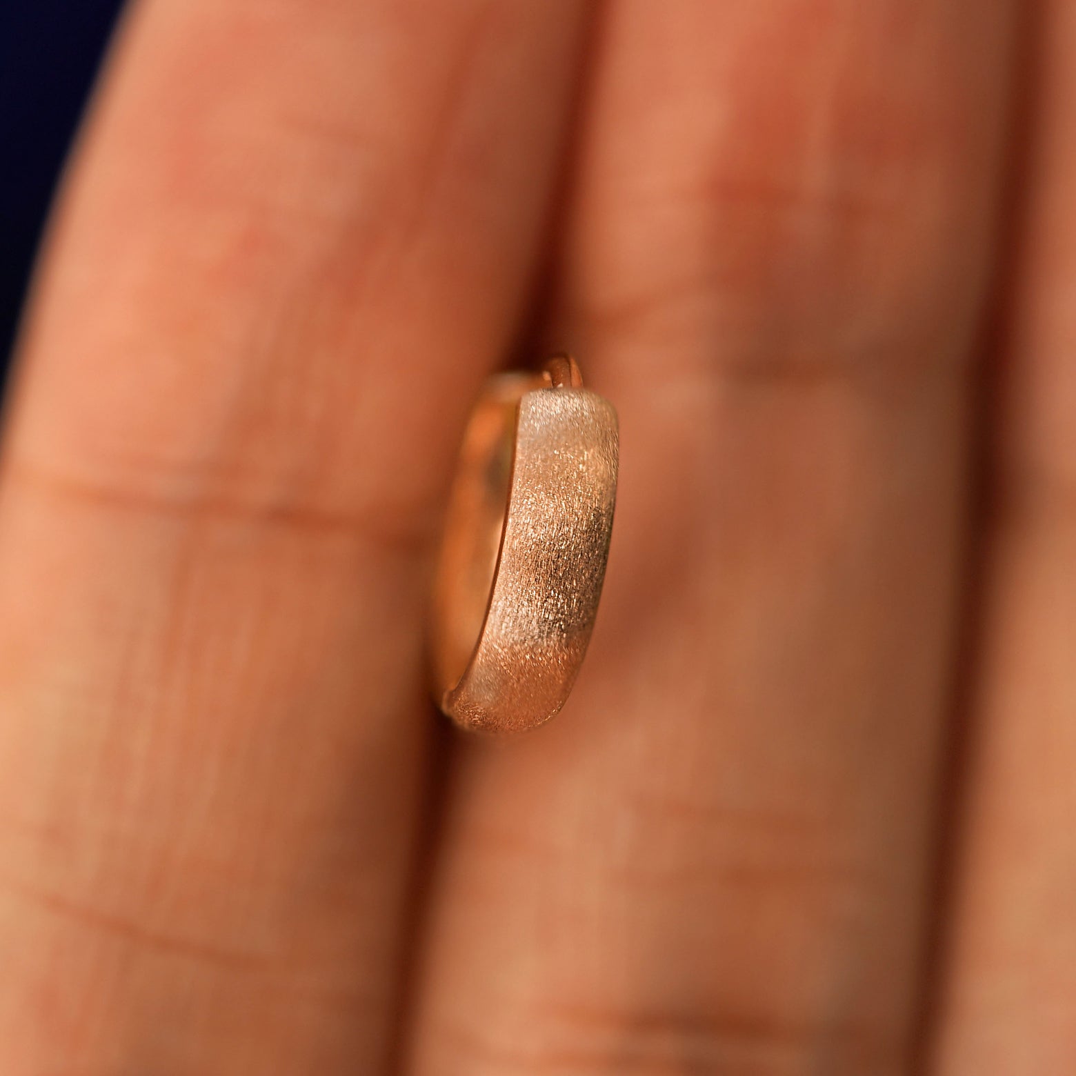 A rose gold Stardust Small Thick Huggie Hoop Earring held in between a model's fingers to show the hoops thickness