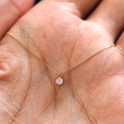 A solid 14k gold Rose Quartz Necklace resting in a models palm