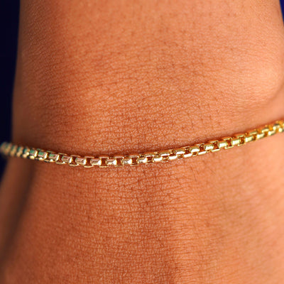 Close up view of a model's wrist wearing a yellow gold Round Box Chain Bracelet