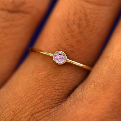 Close up view of a model's fingers wearing a solid yellow gold gemstone Pink Sapphire Ring
