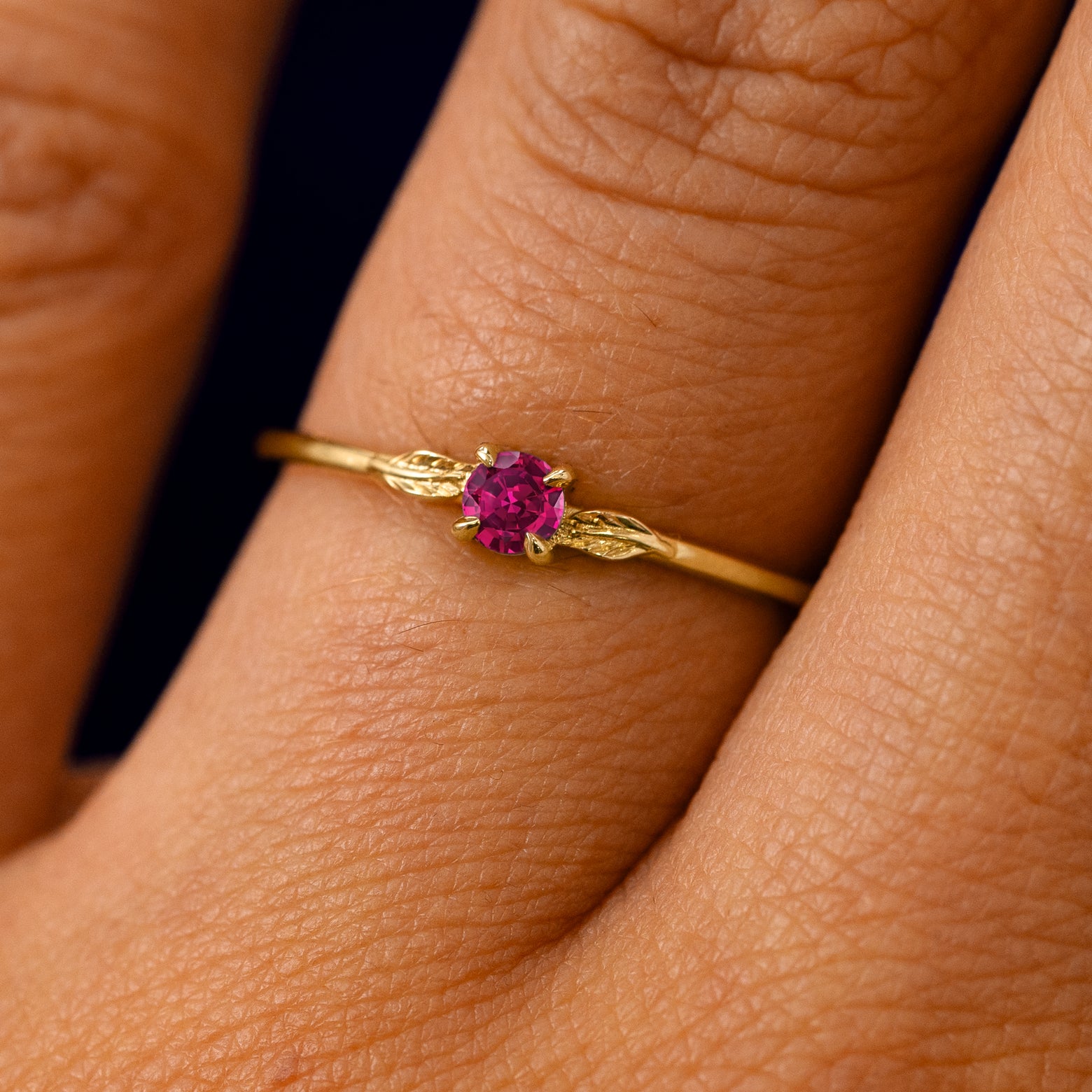 A solid 14k yellow gold Ruby Gemstone Two Leaf Ring on a model's finger