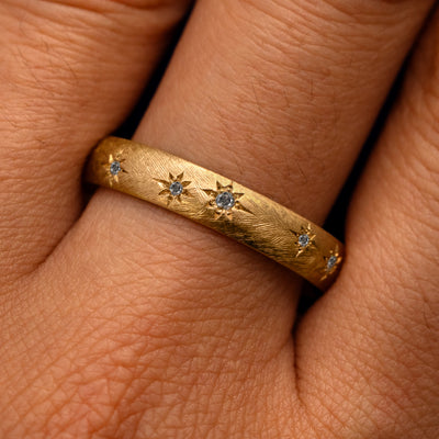 Close up view of a model's fingers wearing a 14k yellow gold Curvy Salt and Pepper Diamond Stars Velvet Band