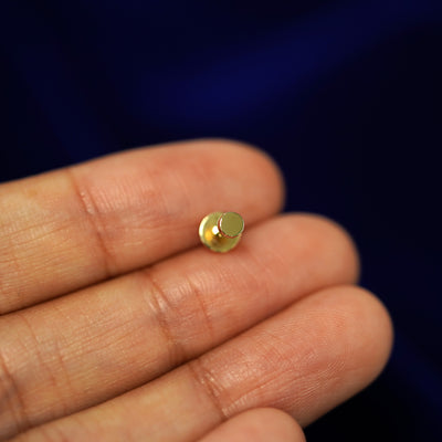 A solid yellow gold Screw Flatback Piercing laying facedown on a model's finger to show the end of the flat back