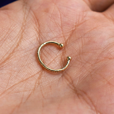 A solid 14 karat yellow gold Shimmer Line Cuff earring resting on a model's palm