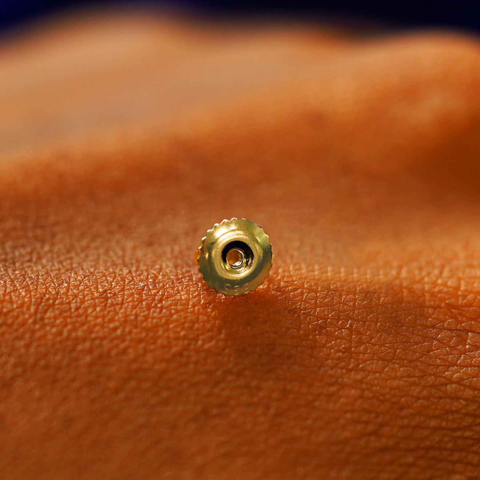 A single solid 14k gold screw back earring backing on the back of a hand
