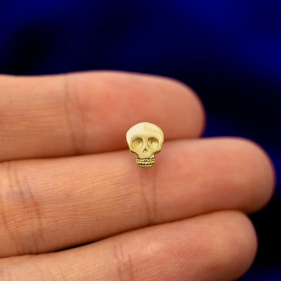 A model holding a solid gold skull stud earring between two fingers