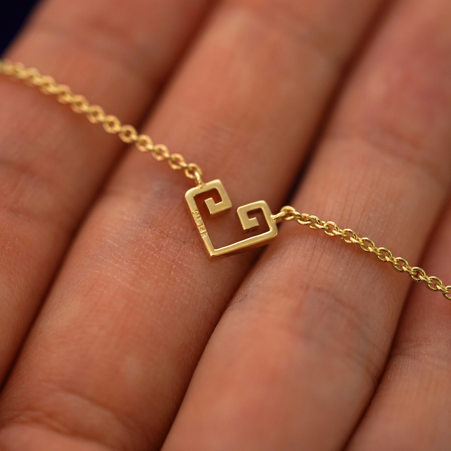 The back of a solid gold Small Chere Heart Necklace resting on a model's fingers to show the stamps
