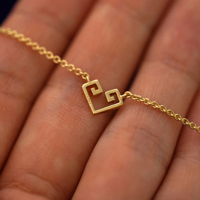 The back of a solid gold Small Chere Heart Necklace resting on a model's fingers to show the stamps