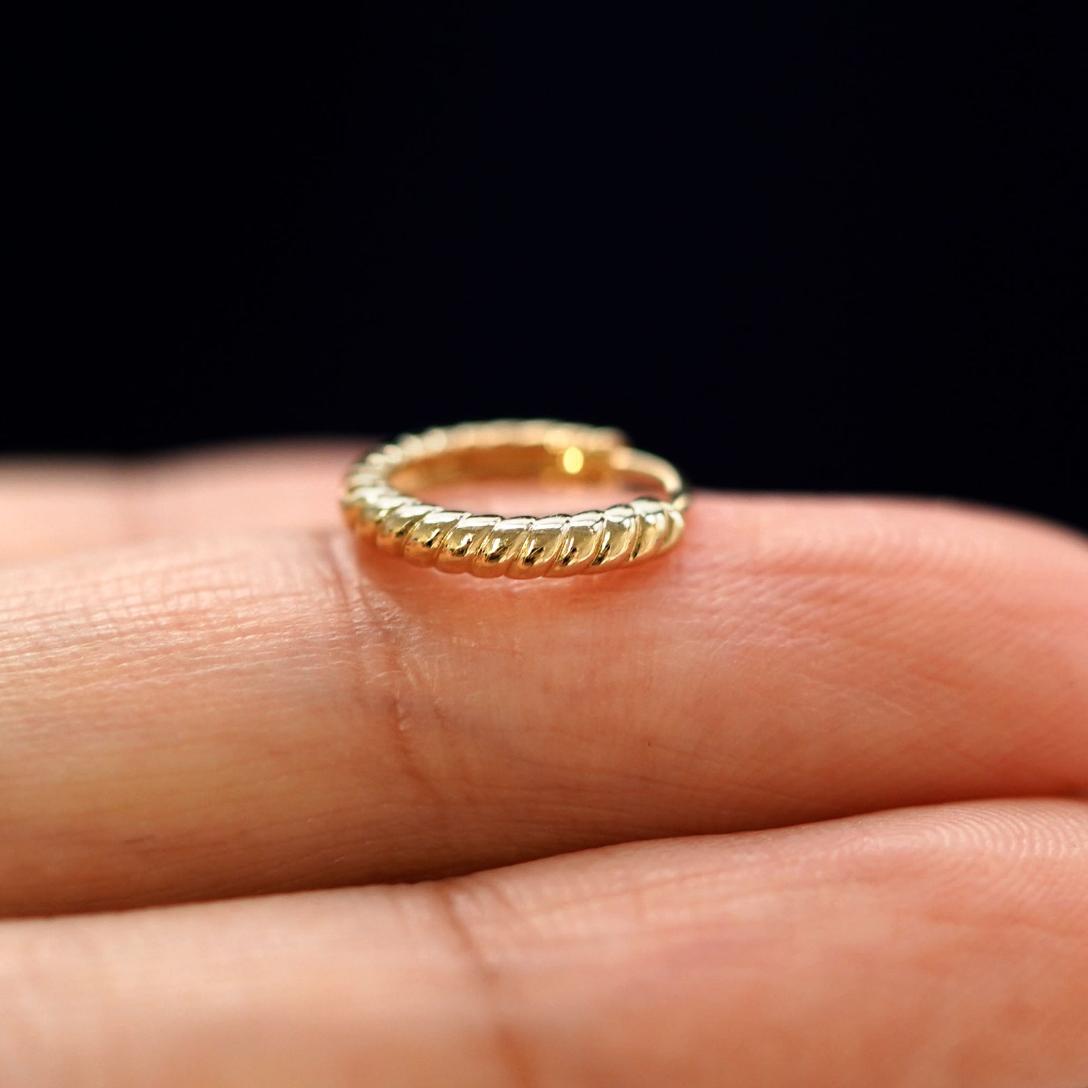 A yellow gold Small Rope Huggie Hoop Earring laying sideways on a model's fingertips
