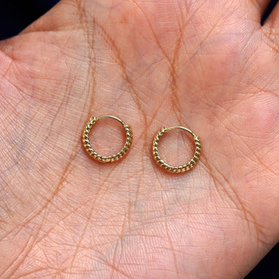 A pair of 14k gold Small Rope Huggie Hoop Earring sitting in a model's palm