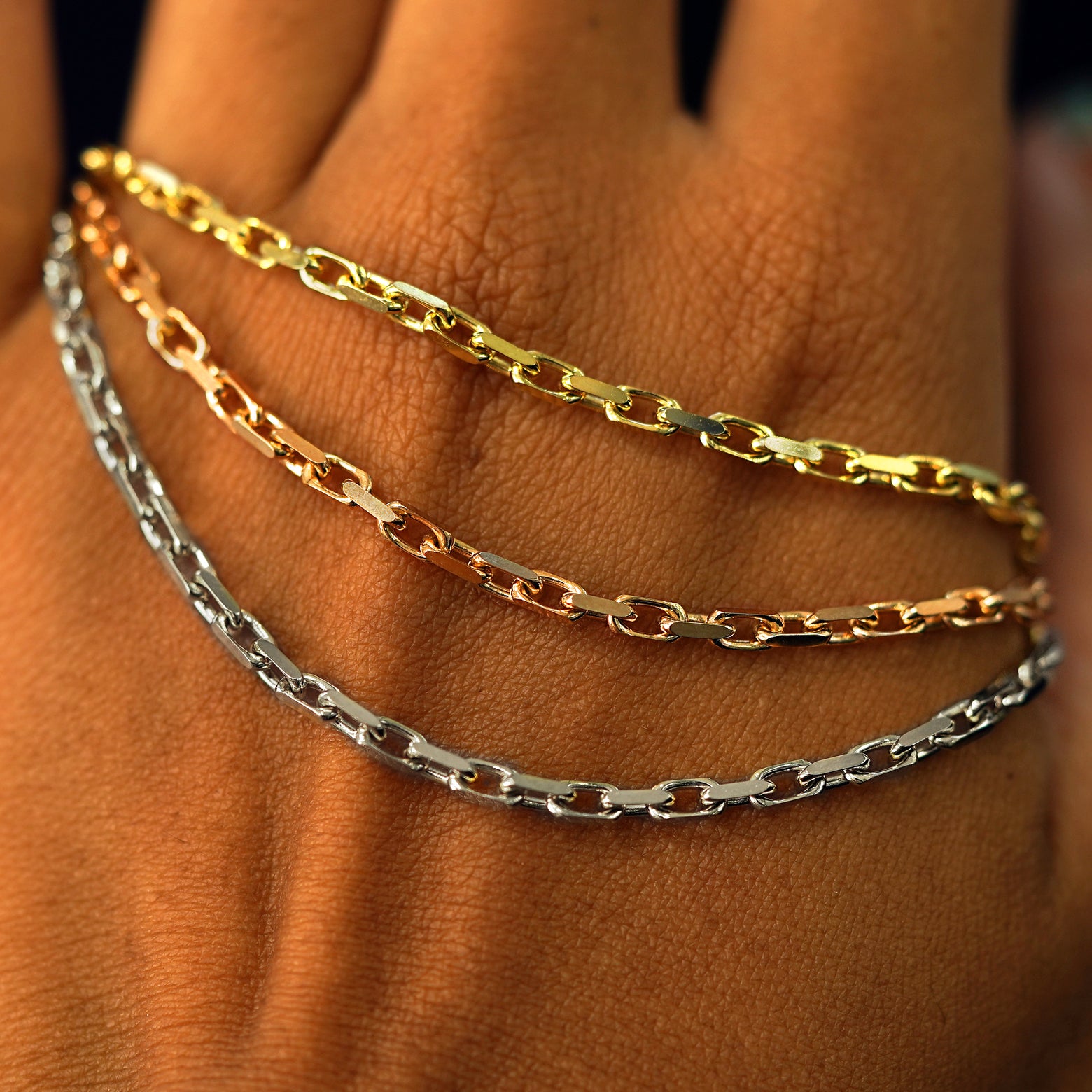 Close up view of a model's hand holding three versions of the Anchor Necklace in yellow, rose, and white gold