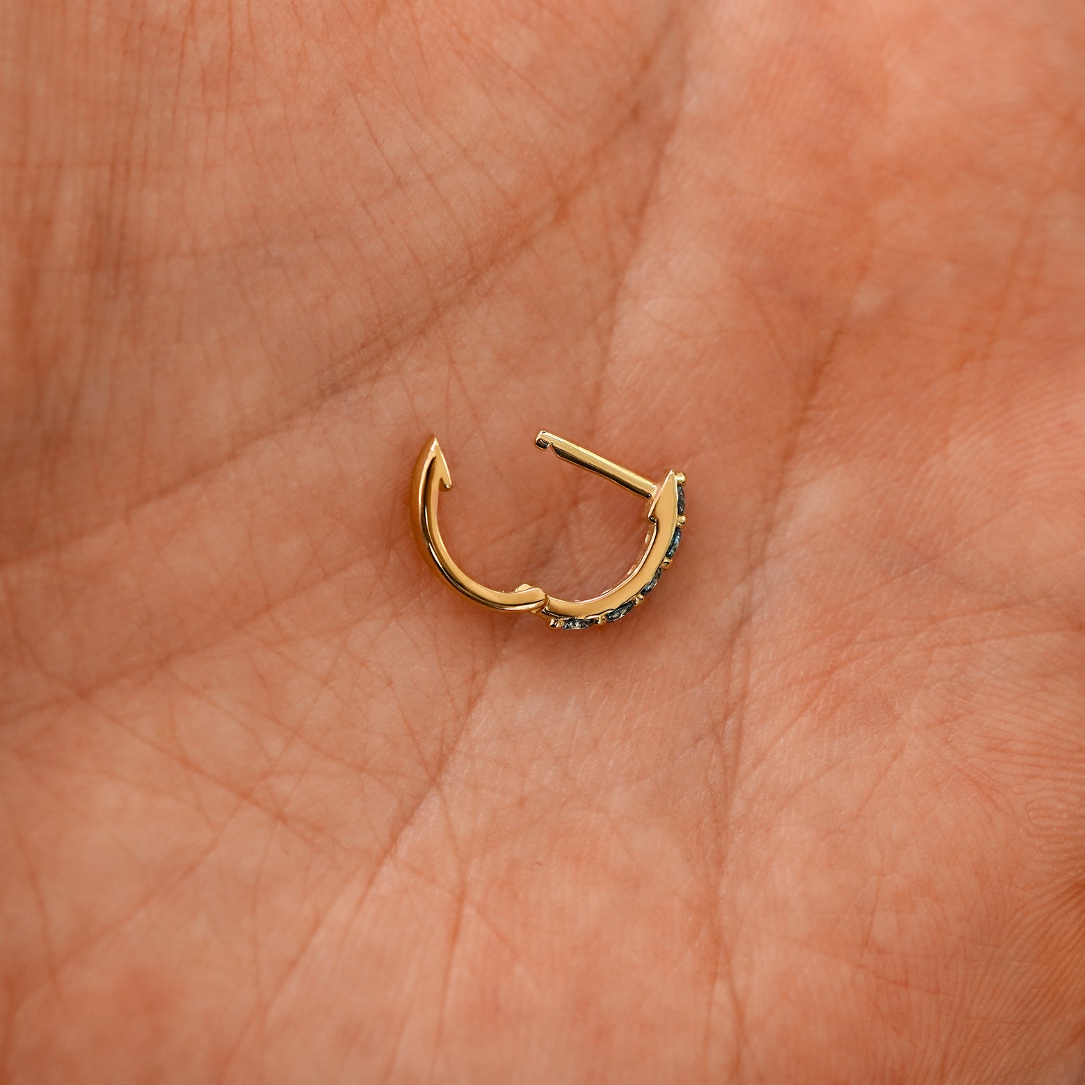 An open lab light blue diamond huggie hoop laying in a models palm