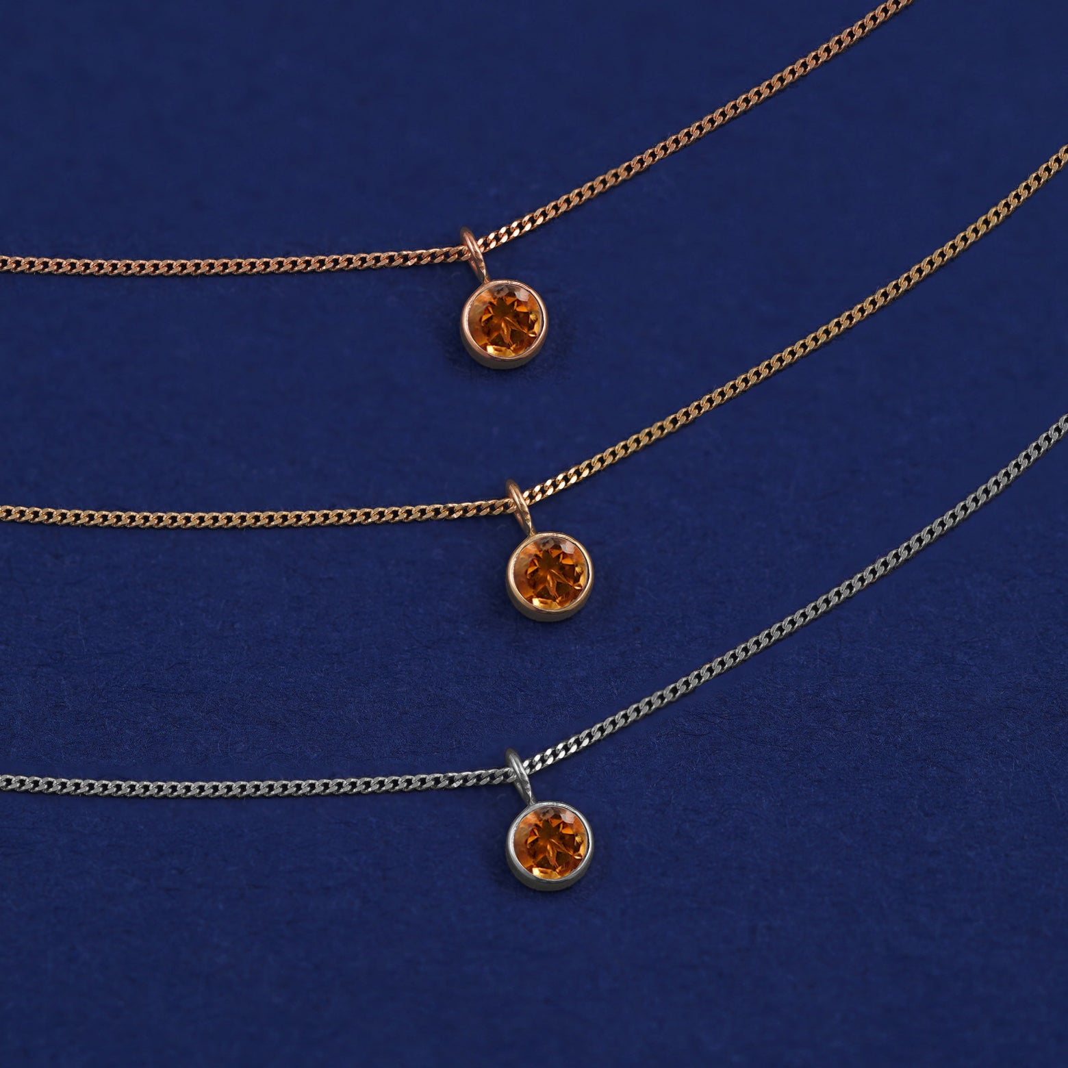 Three versions of the Citrine Necklace shown in options of yellow, white and rose gold on a dark blue background
