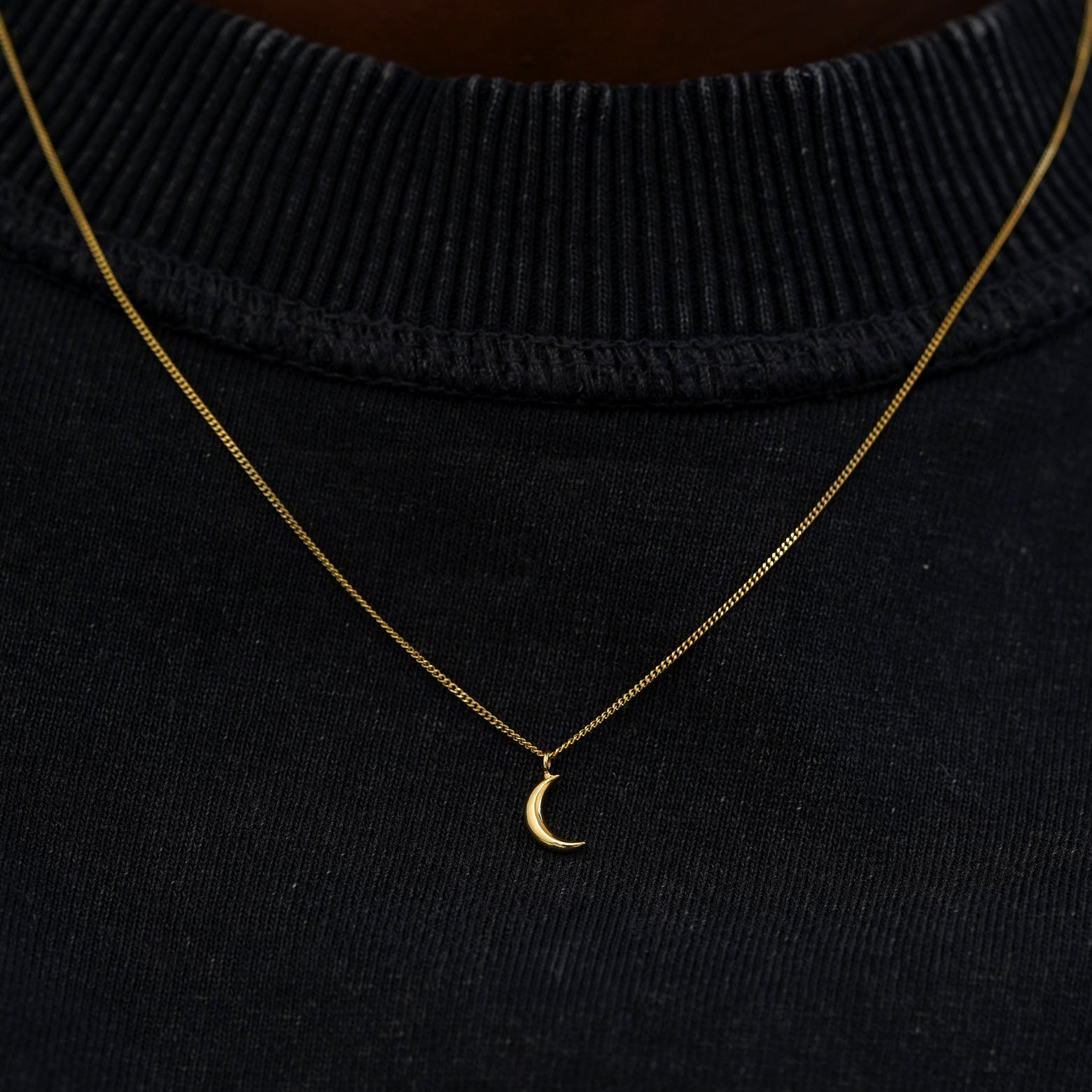 A solid 14 karat gold moon necklace against a model's black shirt