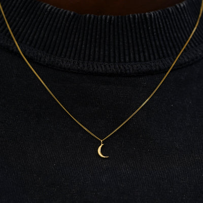 A solid 14 karat gold moon necklace against a model's black shirt