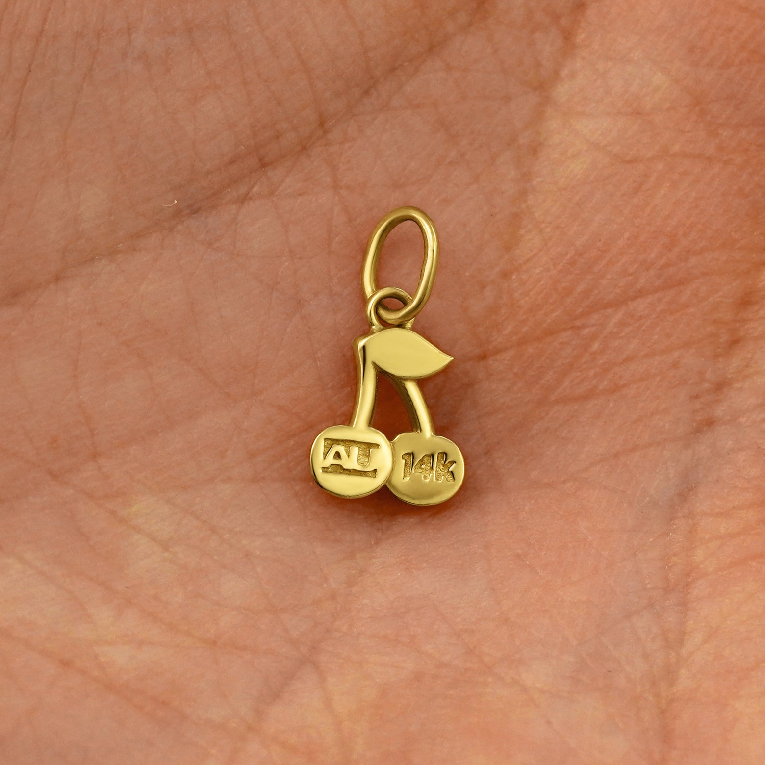 Back view of a solid 14k yellow gold Cherry Charm resting on in the palm of a model's hand