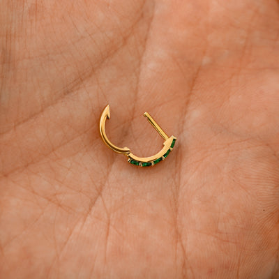An open Emerald huggie hoop laying in a models palm