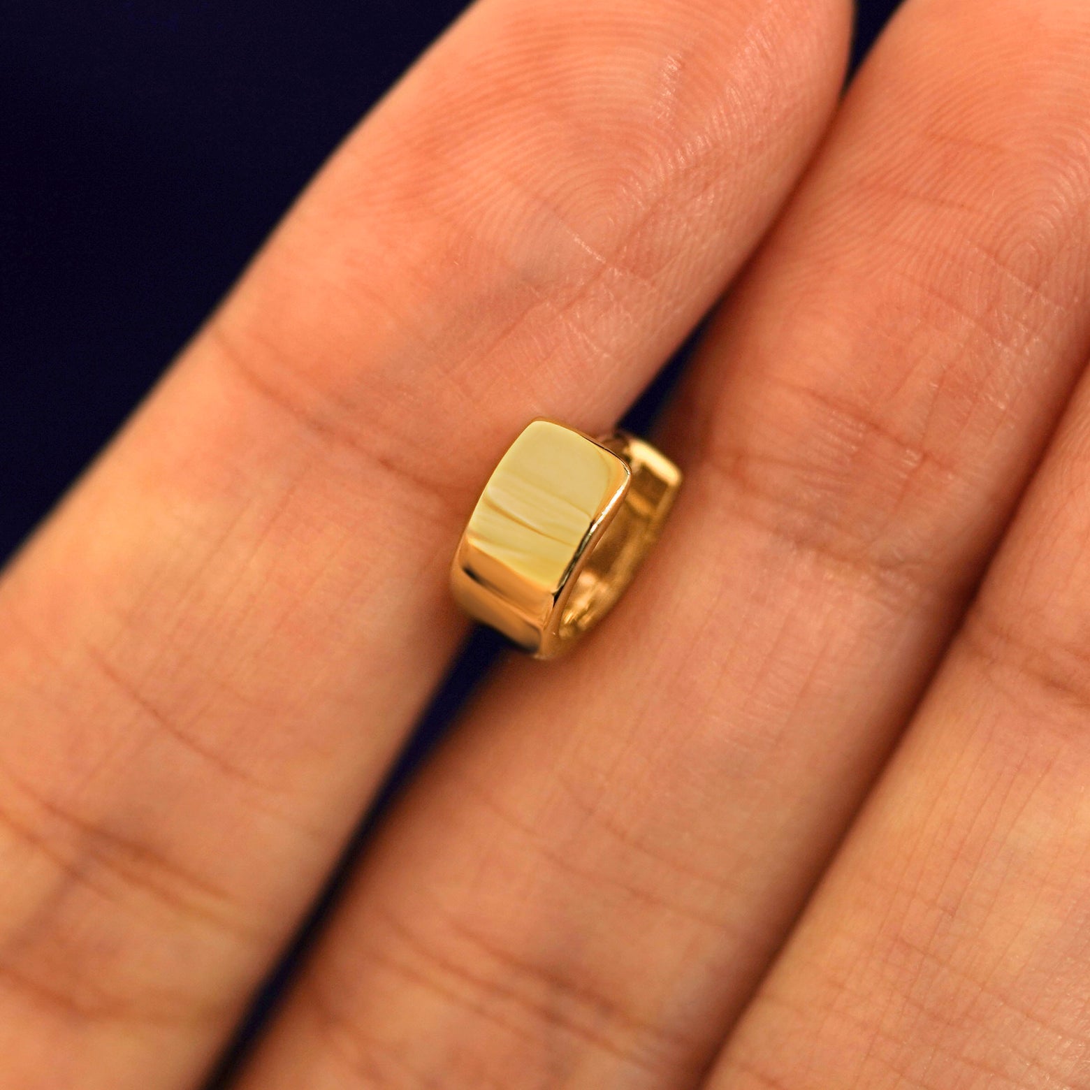 A 14k solid gold Extra Wide Huggie Hoop between a model's fingers to show the thickness of the earring